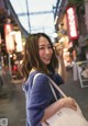 A woman in a blue sweater holding a white bag.