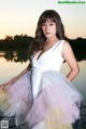 A woman in a white dress standing by a body of water.