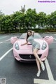 A woman sitting on top of a pink sports car.