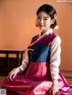 A woman in a pink and blue hanbok sitting on the floor.