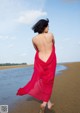A woman in a red dress walking on the beach.