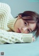 A young woman laying on a blue surface wearing a white sweater.